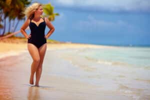 Woman with curvy proportions after fat transfer walks down the beach confidently.