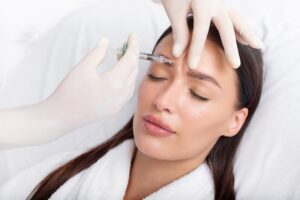 Young woman receiving anti-aging Botox injection to forehead from professional cosmetologist in beauty salon